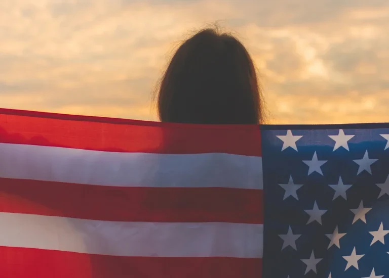 a woman holding an american flag in front of a cloudy sky